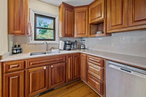 A kitchen with wooden cabinets, a stainless steel sink, a Bosch dishwasher, and a window with a view of trees. - Secluded Riverfront Estate with 180 Degree views-Hot Tub, Fire Pit, Kayaks (New Bern)