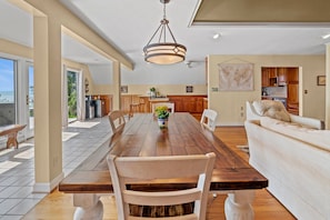 A spacious dining area with a long wooden table, white chairs, and a hanging light fixture. - Secluded Riverfront Estate with 180 Degree views-Hot Tub, Fire Pit, Kayaks (New Bern)
