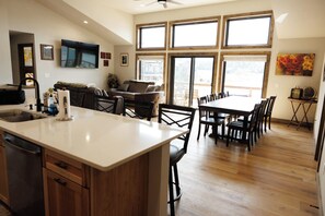 A modern kitchen with a central island, dining area with chairs, and large windows. - Rustic Retreat | Fall Lake Retreat | Fire Pit, Kayaks & Paddleboards (New Lisbon)