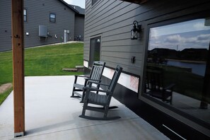 Eine Terrasse mit zwei Schaukelstühlen und einem Betonboden, angrenzend an ein Gebäude mit großen Fenstern und Blick auf ein Gewässer.