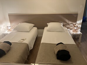 A hotel room with two single beds, each with a pillow and a bedside table with a lamp. - At Germaine: Air-Conditioned Apartment with Ocean View (Six-Fours-les-Plages)