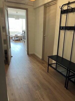 A hallway with wooden flooring, a bench, a coat rack, and a door leading to a dining area. - At Germaine: Air-Conditioned Apartment with Ocean View (Six-Fours-les-Plages)