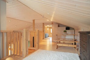 Une pièce mansardée spacieuse avec des poutres apparentes, une moquette blanche et un lit à l’arrière-plan.