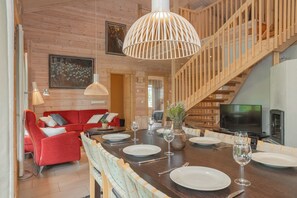 Un intérieur en bois avec une table à manger dressée pour six personnes, un canapé rouge et un escalier.