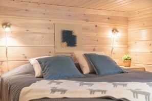 A wooden cabin bedroom with a bed, pillows, a wall-mounted light, and a small plant. - Villa Lumikenkä – Cozy Retreat & Private Sauna (Kuusamo)