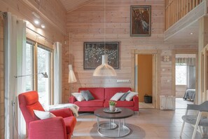 A spacious living room with a red sofa, a round coffee table, and a large painting on the wall. - Villa Lumikenkä – Cozy Retreat & Private Sauna (Kuusamo)