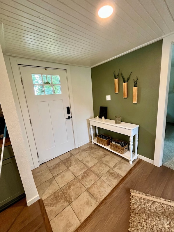 A hallway with a white door, a white console table with baskets, and a green wall with three wooden vases.