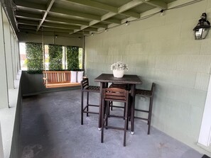 A covered outdoor seating area with a table and chairs, a hanging light fixture, and a potted plant.