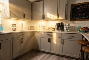 A kitchen with white cabinets, a coffee machine, and a chalkboard with 'WELCOME TO Sand & Paradise' written on it. - Saltwater Heated Pool | Kayaks |Golf Cart | Firepit | Beach (Palm Coast)