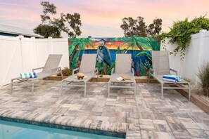 A poolside area with lounge chairs and a mural in the background. - Saltwater Heated Pool | Kayaks |Golf Cart | Firepit | Beach (Palm Coast)