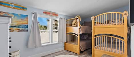 Une pièce avec deux lits superposés, un ventilateur de plafond, une fenêtre avec des rideaux, un tableau et un petit tapis.