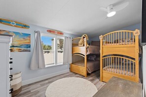 A room with two bunk beds, a ceiling fan, a window with curtains, a painting, and a small rug. - Saltwater Heated Pool | Kayaks |Golf Cart | Firepit | Beach (Palm Coast)