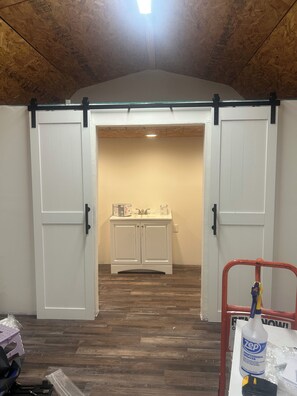 A room with a wooden ceiling, a white cabinet with a sink, and a red metal cart with cleaning supplies.
