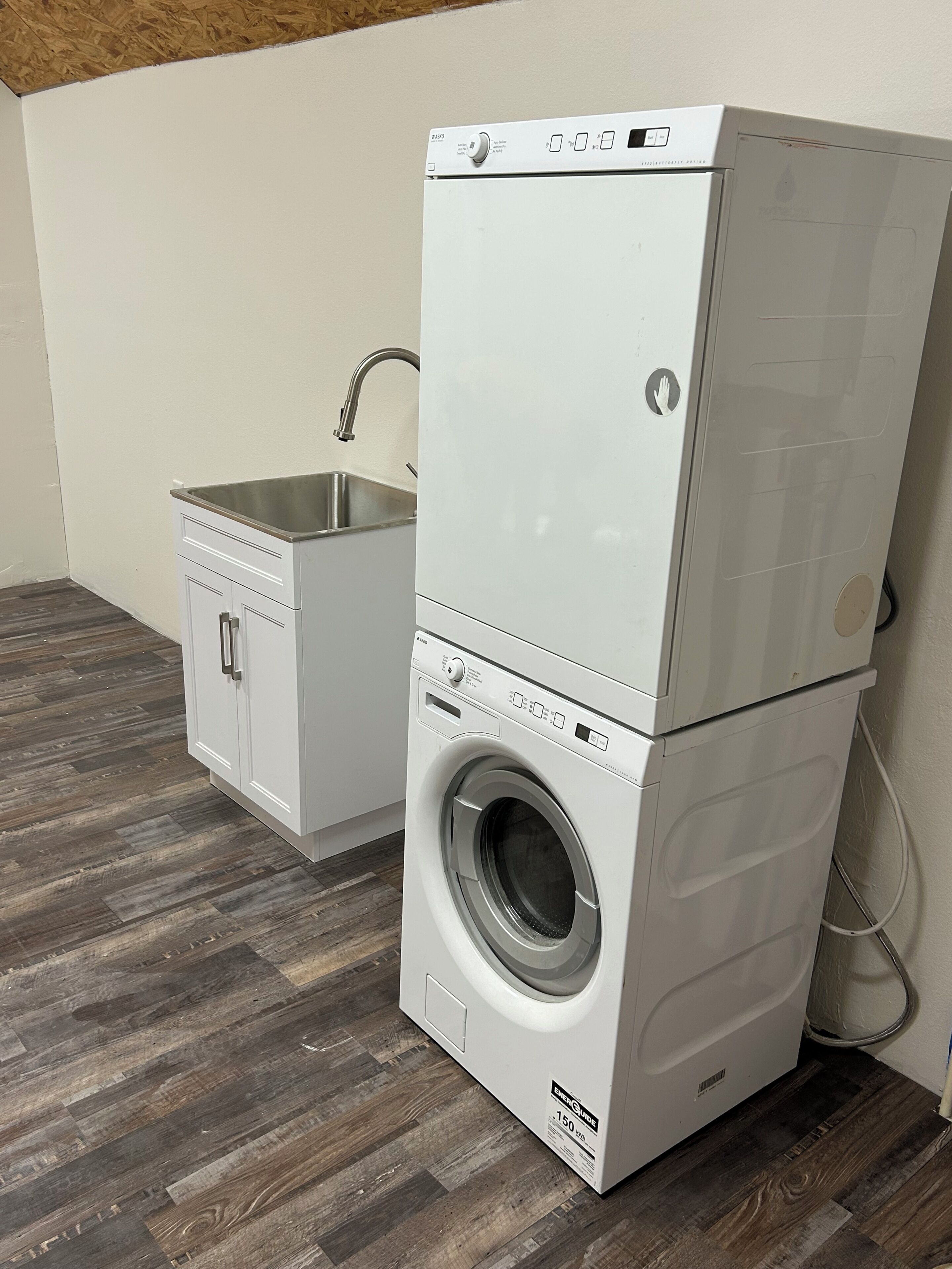 A stacked washer and dryer unit with a small sink and cabinet.