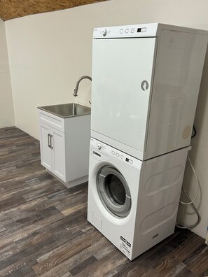A stacked washer and dryer unit with a small sink and cabinet.
