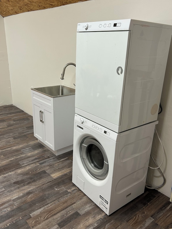 A stacked washer and dryer unit with a small sink and cabinet.