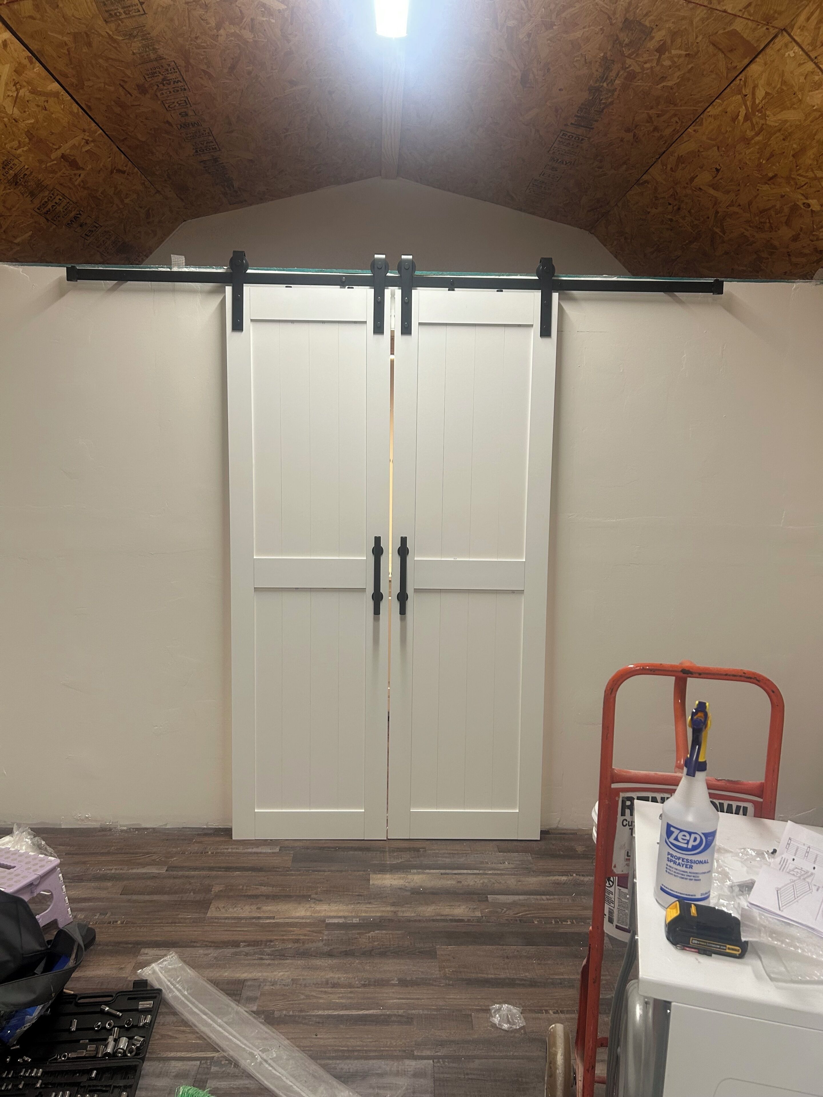 Een kamer met een houten plafond, een witte deur met een zwarte handgreep, een rode stoel en een gereedschapskist op de vloer.