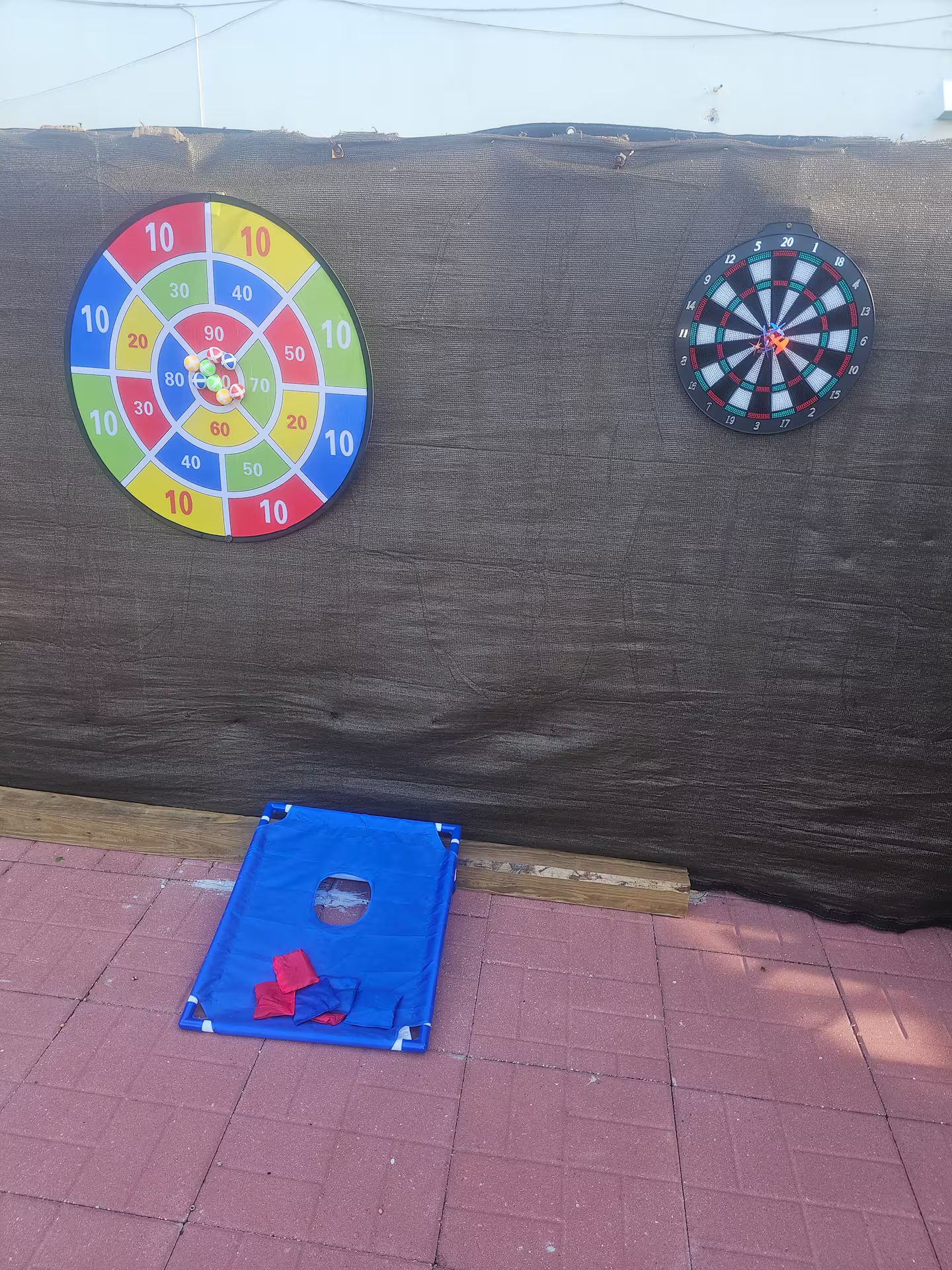 Dos dardos colgados en una pared texturizada, una alfombra azul con cuadrados rojos en el suelo, y una estructura de madera parcialmente visible.