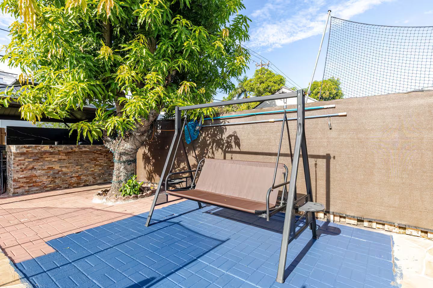 A backyard with a swing set, a brick patio, and a tree.