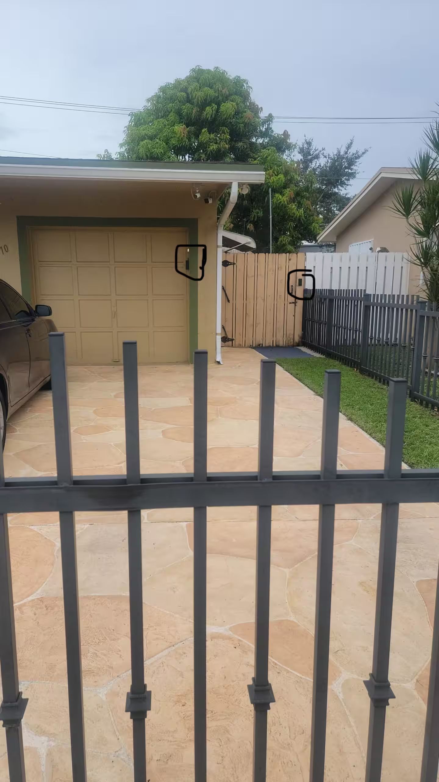 A residential garage with a car parked inside, a covered driveway, and a fenced backyard.