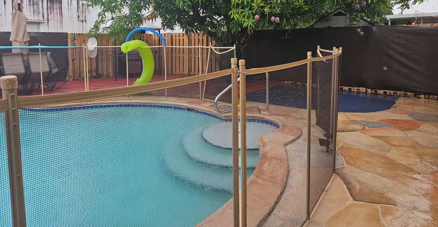 An indoor swimming pool with a safety fence, a slide, and a stone-tiled floor.