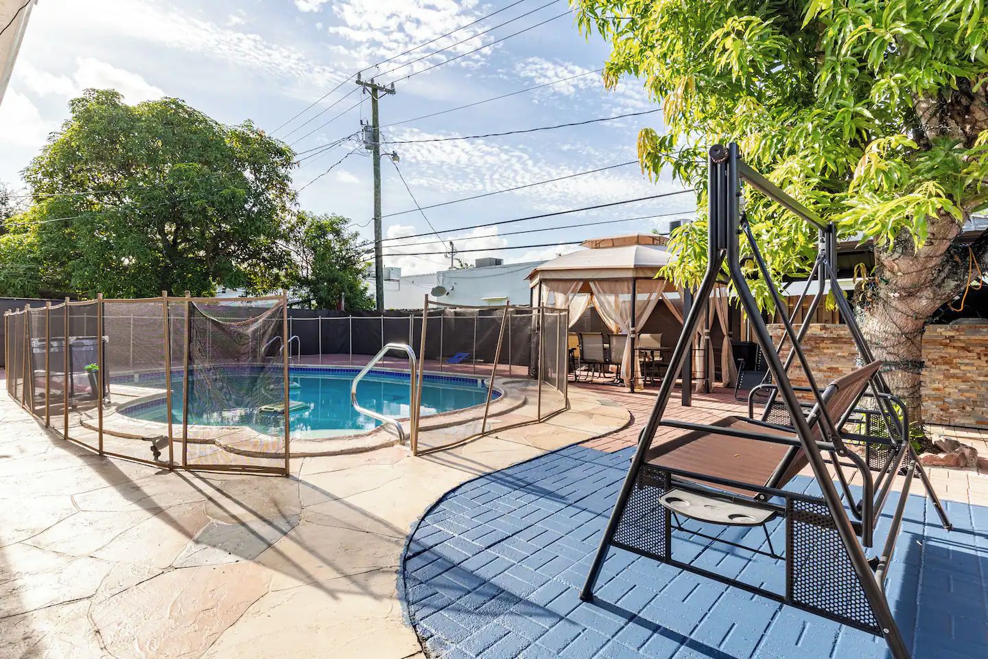 A backyard with a swimming pool, a covered seating area, and a swing set.