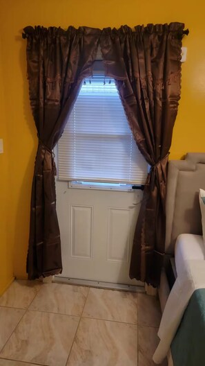 A room with a door, a window with blinds, and a sofa. - Sunrise Efficiency (Sunrise)