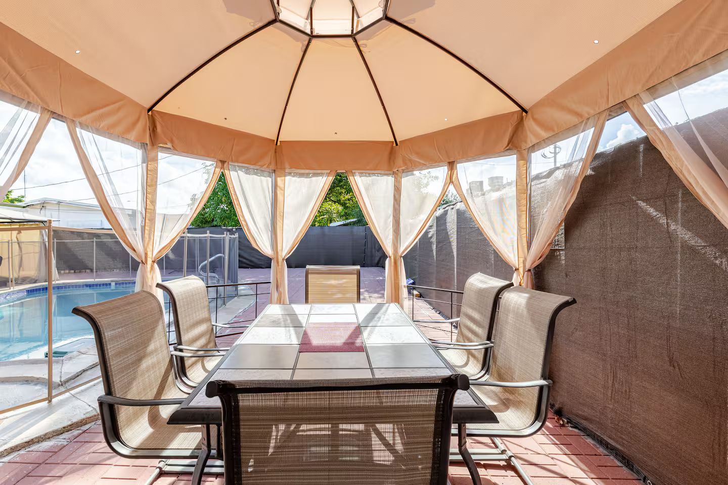 A covered outdoor seating area with a pool in the background.