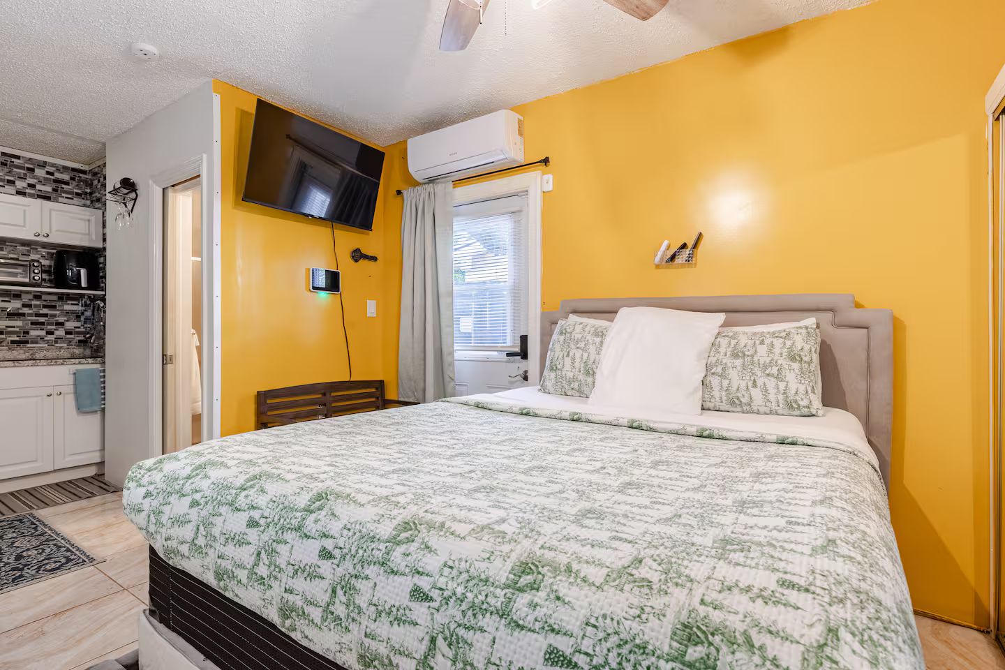 Une chambre à coucher avec un lit, un téléviseur fixé au mur et une fenêtre avec des stores.