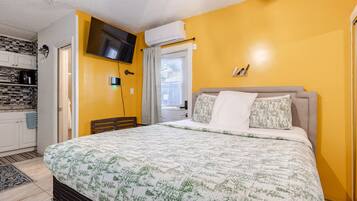 A bedroom with a bed, a television mounted on the wall, and a window with blinds.