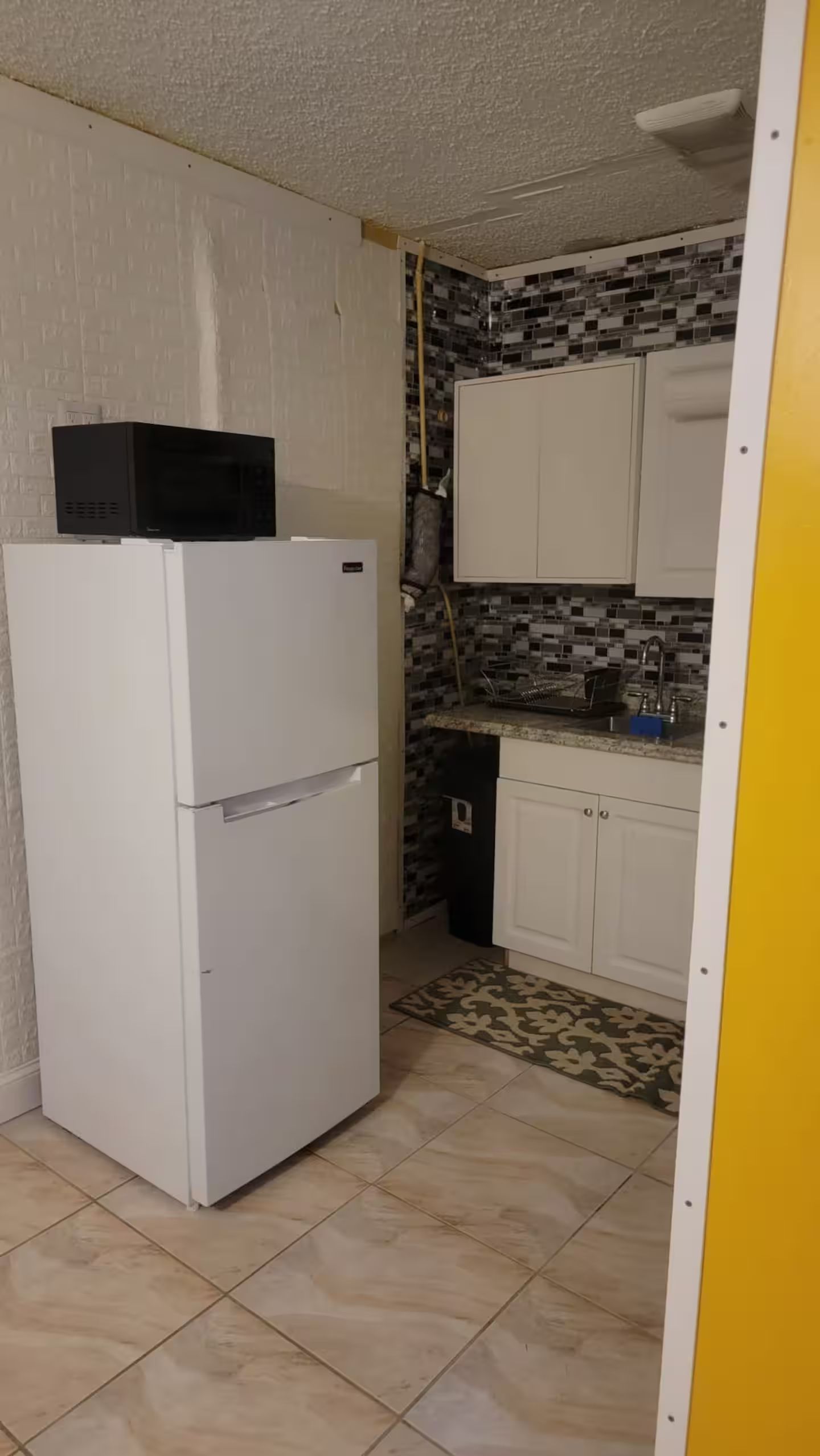 Una cocina compacta con un refrigerador blanco, salpicadero de azulejos y armarios blancos.