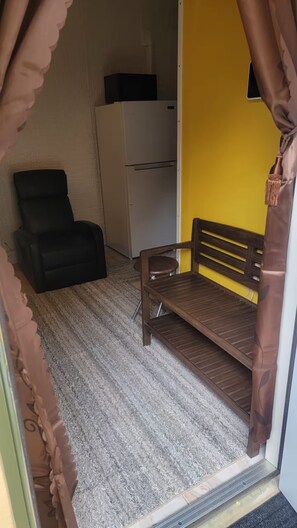A room with a bed, a chair, a small table, and a refrigerator. - Sunrise Efficiency (Sunrise)
