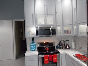 A modern kitchen with white cabinets, a stainless steel microwave, and a red kettle on the stove. - Great Panoramic View Apartment B, Whale Hill. (Puerto Peñasco)