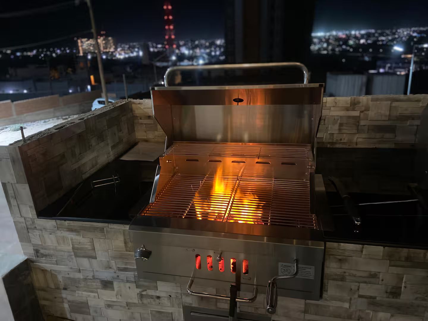Een buitenbarbecue met een digitaal display, voor een stadsgezicht bij nacht.