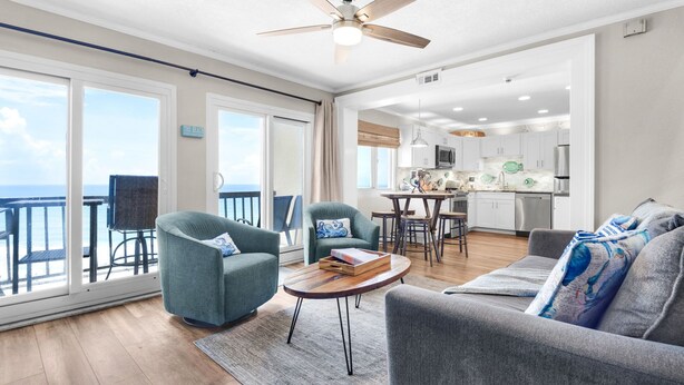 A spacious living area with a balcony, a dining table, and a kitchen in the background. - Ocean Front Livingroom! By 30A, Beautifully Updated, Gated Community, 9th Floor (Panama City Beach)