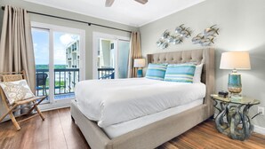 A bedroom with a bed, a ceiling fan, a balcony with a chair, and a decorative wall piece. - Ocean Front Livingroom! By 30A, Beautifully Updated, Gated Community, 9th Floor (Panama City Beach)