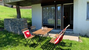Ett utomhusområde med sittplatser, ett bord och stolar, en stenmur och en byggnadsingång med glasdörrar.