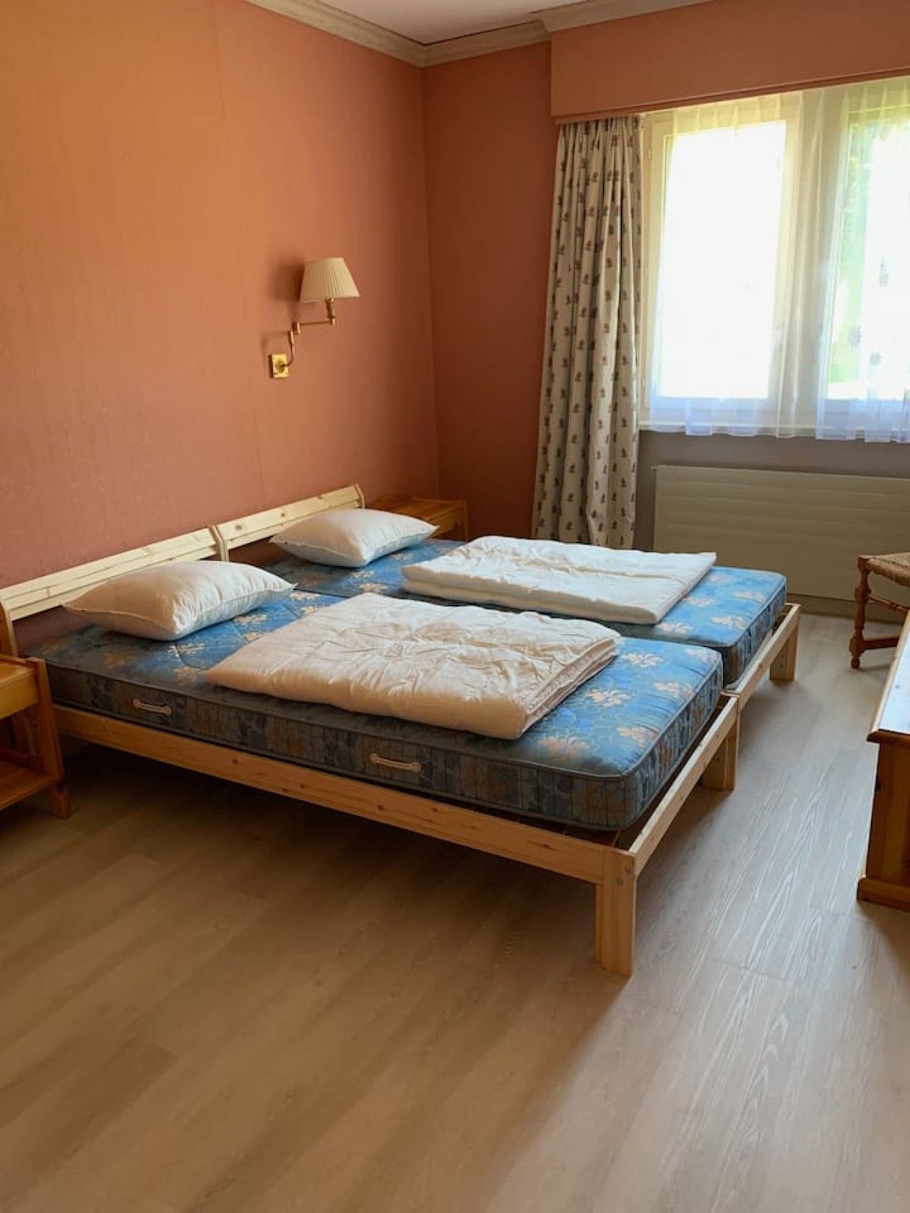 A room with a wooden bed, a bedside table, a lamp, and a window with curtains.