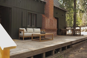 Una terraza de madera con mobiliario exterior, una chimenea de ladrillo y vistas a zona boscosa.