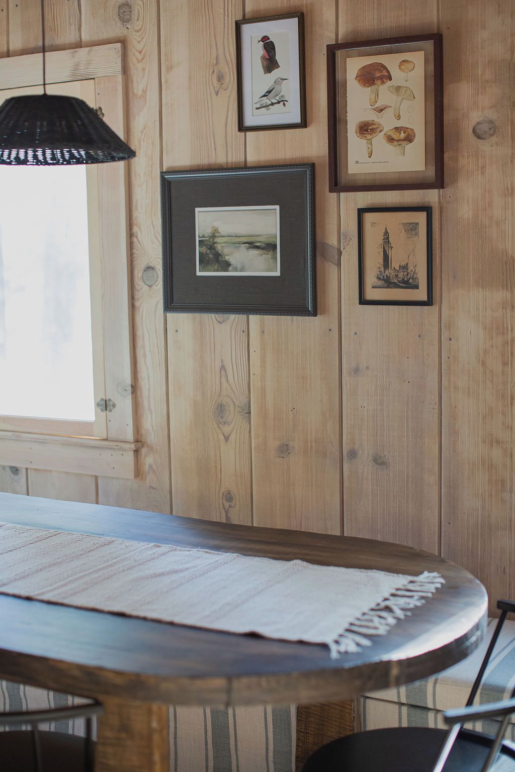 A wooden wall with framed artwork, a table with a placemat, and a hanging pendant light.