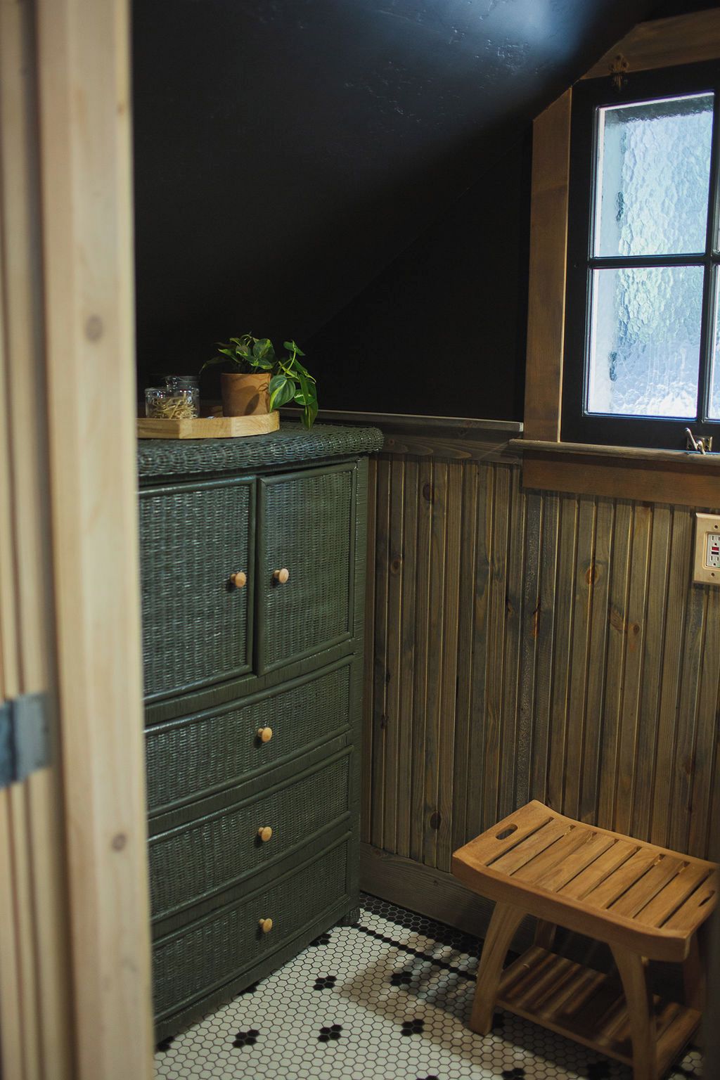 A small room with a green cabinet, a wooden bench, and a window with a view of the outside.