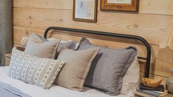 A wooden-paneled room with a bed, pillows, a nightstand, and framed artwork on the wall.
