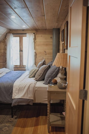 Un dormitorio acogedor con una cama de madera, una mesita de noche con lámpara y una ventana con cortinas.