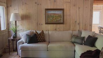 A cozy living room with a beige sofa, a framed painting, a lamp, and a small table with a plant.