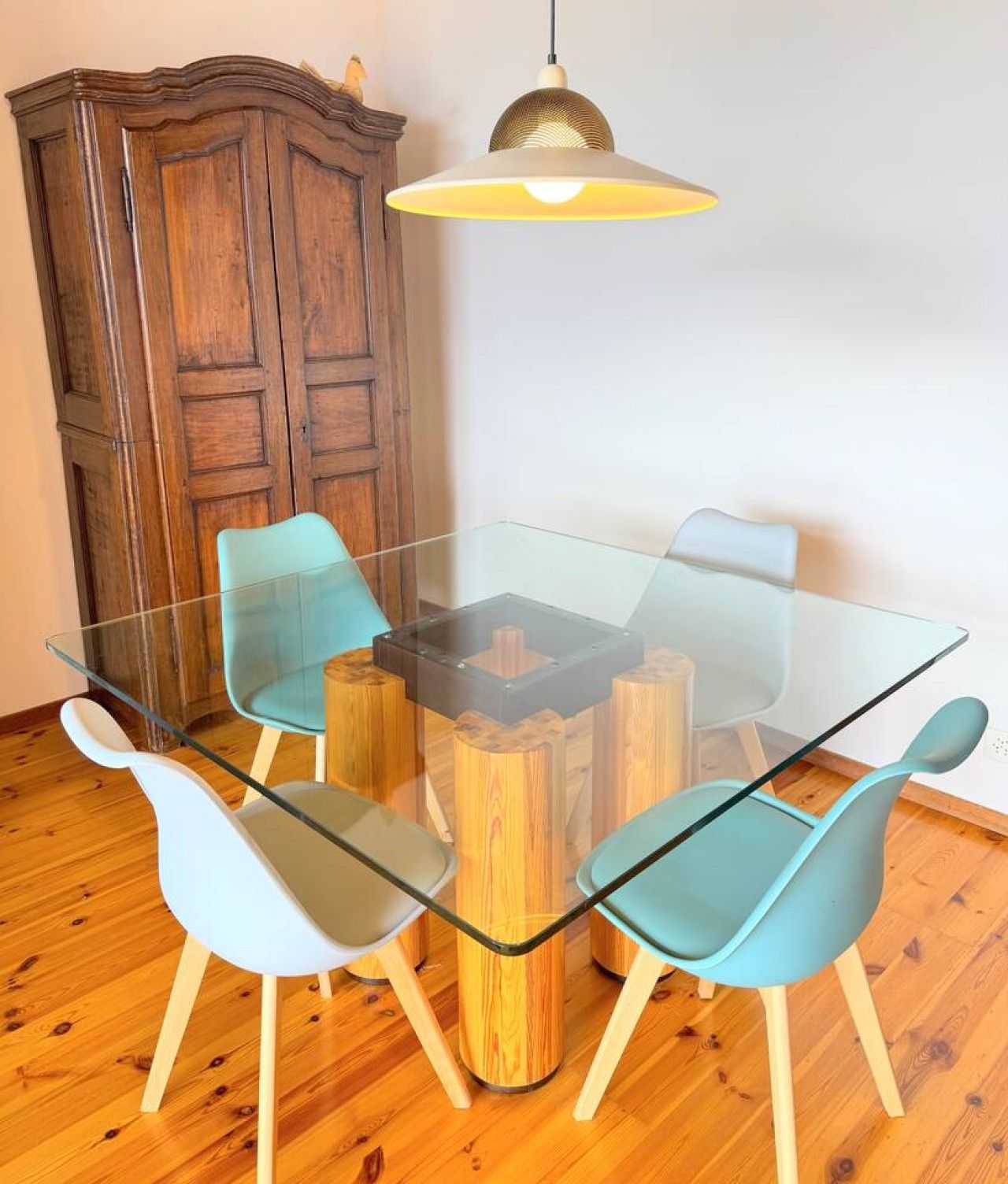 Un comedor con una mesa de vidrio rodeada de sillas, un aparador de madera y una lámpara colgante.