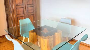 Un comedor con una mesa de vidrio rodeada de sillas, un aparador de madera y una lámpara colgante.