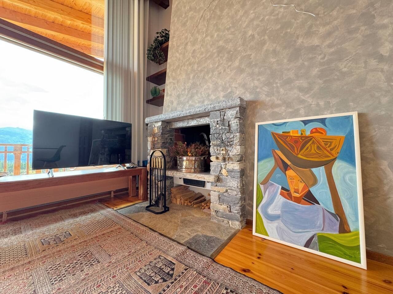 Una sala de estar con chimenea de piedra, un televisor, un cuadro y un ventanal grande.