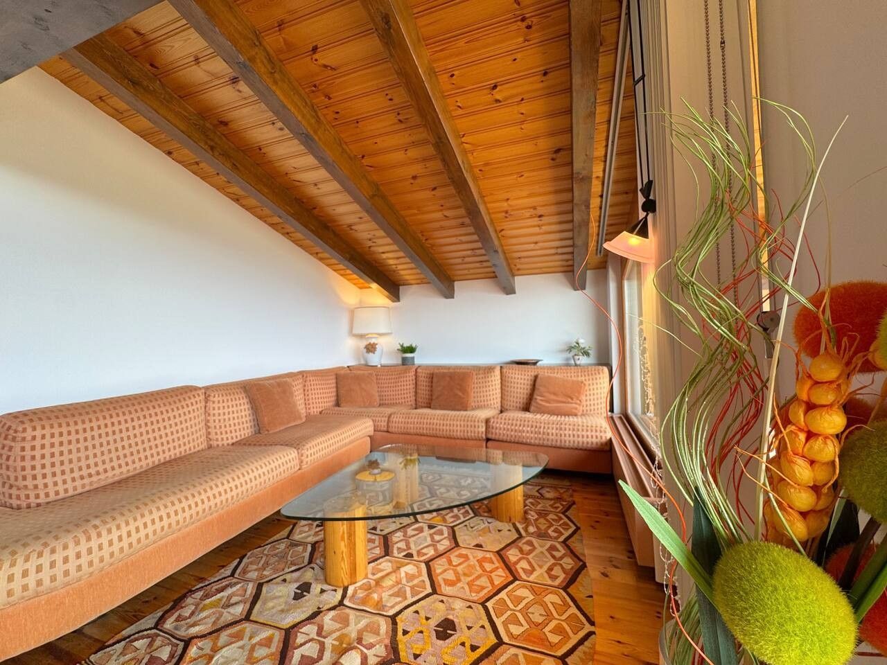 Una sala de estar con techo de madera, alfombra estampada, mesa de centro de vidrio y un sofá.