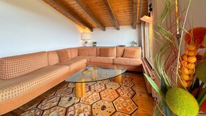 Un soggiorno con soffitto in legno, tappeto decorato, tavolino in vetro e divano.