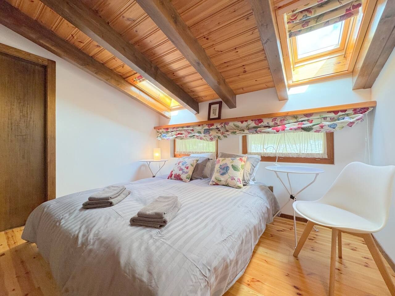 Une chambre avec un grand lit, une chaise blanche et une lucarne.